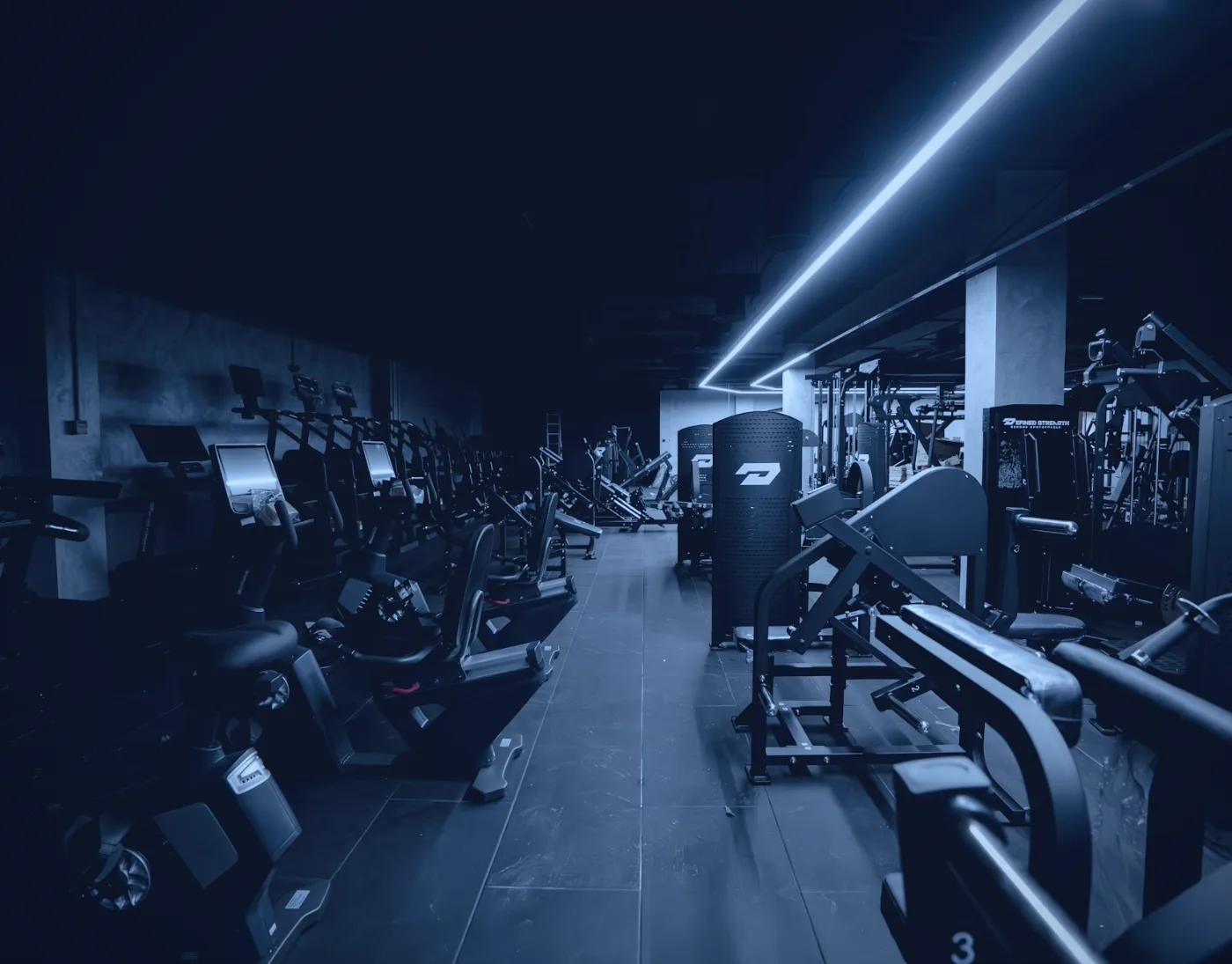 Dark modern gym with rows of exercise machines under blue strip lighting